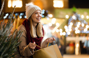 Happy young beautiful woman choosing christmas present and tree at market