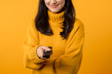 In her comfortable apartment, a young Asian woman in a yellow sweater enjoys watching TV with a...