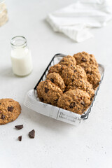 Homemade gluten free oatmeal cookies with banana, dark chocolate and nuts in metallic basket on white concrete background, top view. Healthy eating, ancient grain food concept. Oatmeal biscuit recipe