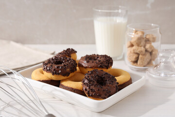 Chocolate donuts on plate, glass of milk and jar of sugar on white wooden background