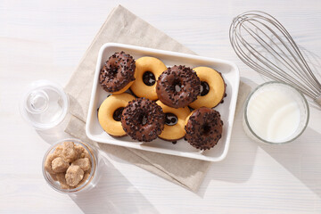 Chocolate donuts on plate, glass of milk and jar of sugar on white wooden background, top view