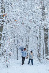 In the winter forest, the couple walks together. the man has a Christmas tree on his shoulder