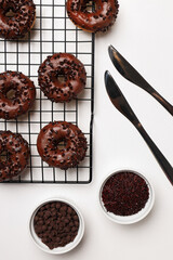Chocolate donuts, bowls and knives on white background, top view