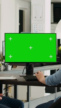 Vertical video Corporate team using greenscreen on monitor while sitting at agency workstation, small business development. Man and woman colleagues looking at display showing isolated copyspace.