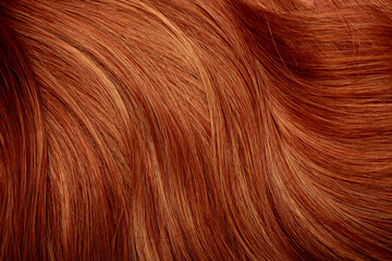 Fototapeta premium Red hair close-up as a background. Women's long orange hair. Beautifully styled wavy shiny curls. Hair coloring bright shades. Hairdressing procedures, extension.