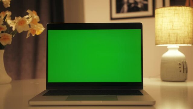 Workplace with laptop on desk with blank empty green mockup screen. Close up shot of modern chroma key green screen laptop computer set up for work on desk at night.