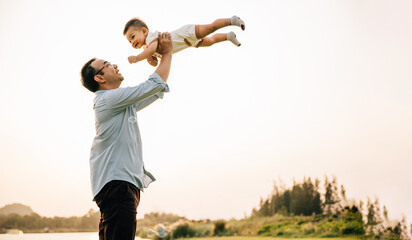 Playful family moment, father holds happy little boy up high, throwing up in sky on his birthday....