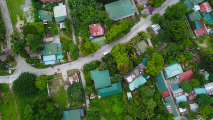 Top view of an asphalt road and roofs of buildings among green trees. Aerial view of a small settlement in the forest. Road, buildings, roofs, forest. © Houston