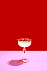 Traditional original drink. Glass with martini decorated with olives isolated over red background. Gin and vermouth taste. Concept of alcohol drinks, party, holidays, bar. Poster. Copy space for ad