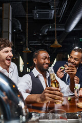 happy and drunk interracial friends drinking tequila and beer in bar after work, male friendship