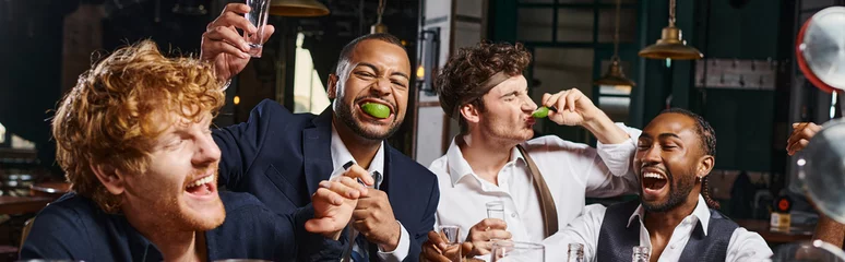 Fotobehang banner of four happy and drunk multiethnic friends in formal wear drinking tequila in bar after work © LIGHTFIELD STUDIOS