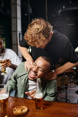 redhead man tickling happy african american groom during bachelor party in bar, male friendship