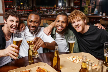 group of happy multiethnic friends hugging and toasting with glasses of beer, spending time in bar