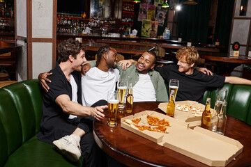 four happy interracial friends hugging and chatting near pizza and beer, spending time in bar