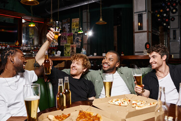 four happy interracial friends raising bottles and glasses of beer in bar, spending time together