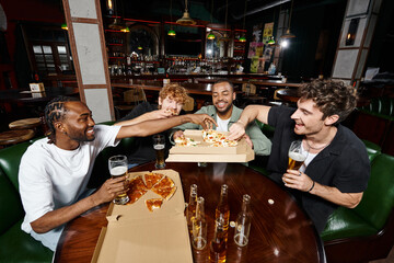 group of four multiethnic friends sharing pizza and drinking beer in bar, men on bachelor party
