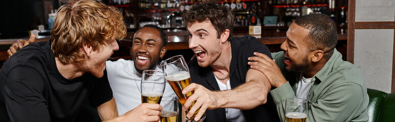 banner of excited multicultural friends clinking with glasses of beer in bar, men on bachelor party