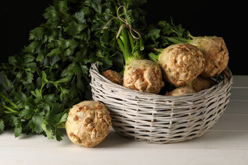 Fresh raw celery roots in wicker basket on white wooden table