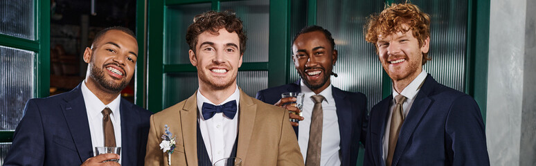 bachelor party banner, happy interracial best men and groom in suits holding glasses of whiskey - obrazy, fototapety, plakaty