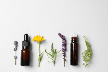 Bottles of essential oils, different herbs and flowers on white background, flat lay. Space for text