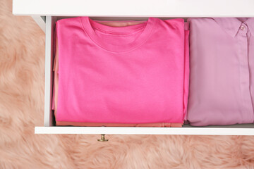 Folded pink clothes in white chest of drawers indoors, top view