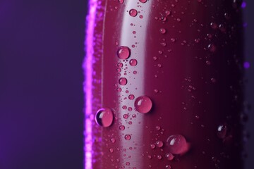 Lipstick with water drops on purple background, macro view. Space for text