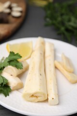 Cut raw salsify roots with parsley and lemon on white plate, closeup
