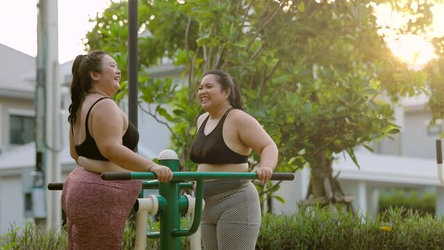 Two beautiful plus size asian woman doing exercise together with exercise machine in the natural garden in the evening.