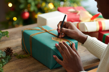 Woman writing Merry Christmas note to add to wrapped present