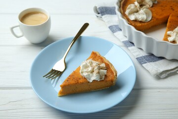 Delicious pumpkin pie with whipped cream, fork and cup of coffee on white wooden table