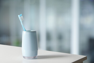 Plastic toothbrush in holder on white table against blurred background, space for text