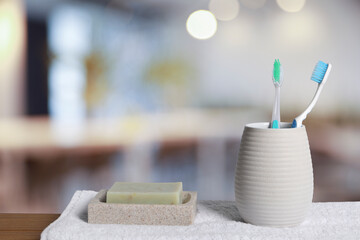 Plastic toothbrushes in holder, soap and towel on wooden table against blurred background, space...