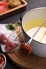 Fondue pot, forks with meat pieces and other products on black textured table, closeup