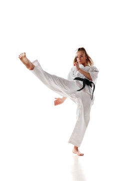 Rear view. Woman professional karate fighter with black belt performing kick in action isolated over white background.