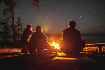 Tourists near a campfire near the shore of Lake Baikal on a starry night. The concept of camping trips with tents to unique places of nature