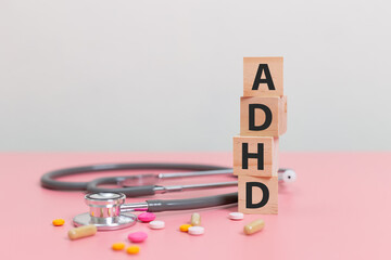 wood cube block Abbreviation of ADHD with Stethoscope and pills on pink table. Attention Deficit Hyperactivity Disorder. ADHD concept.