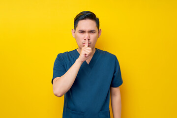 Serious professional young Asian male doctor or nurse wearing a blue uniform showing silent gesture...
