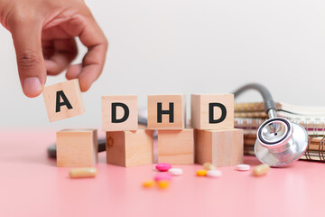 Hand holding wood cube block Abbreviation of ADHD with Stethoscope and pills on pink table. Attention Deficit Hyperactivity Disorder. ADHD concept.