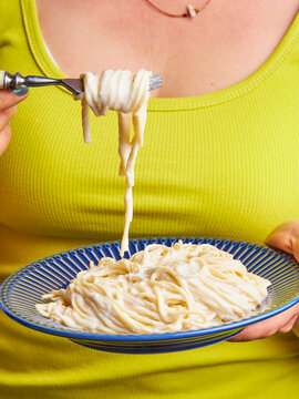 woman with yellow blouse holding a plate of spaghetti with white sauce with a fork