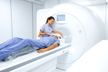 Female radiologist or technician preparing senior man for complete MRI or CT head scan at oncology...