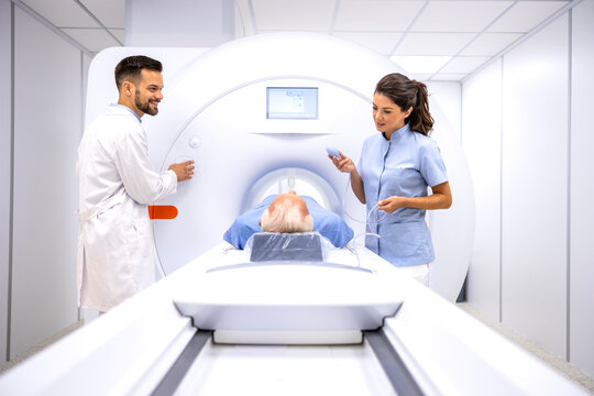 Radiologist and female technician preparing patient for MRI procedure in hospital diagnostic room.