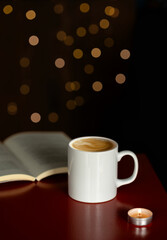 a cup of coffee on the Christmas table with a lit candle and an open book, christmas reading
