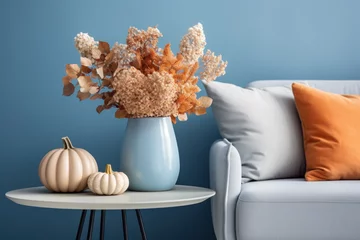 Rolgordijnen A vase with dry hydrangea and pumpkins on the table by the sofa. Autumn living room interior in blue and orange tones. © July P