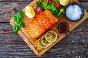 Seared salmon steak with lettuce, tomatoes and lemon on wooden table
