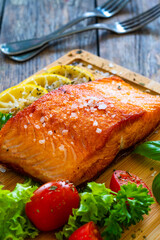 Seared salmon steak with lettuce, tomatoes and lemon on wooden table
