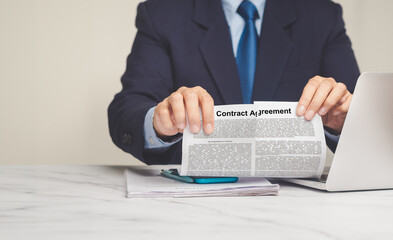 Businessman is tearing up a contract agreement while sitting at the table - obrazy, fototapety, plakaty