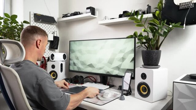 A male photographer connects a graphic tablet to a PC in a home workspace. Technical equipment of the photographer's home office.