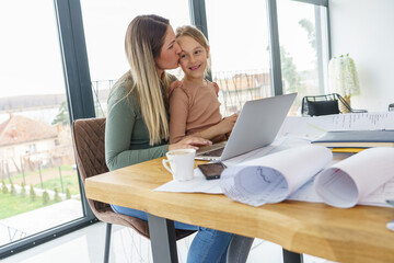 A mother, works from home, surrounded by his supportive family, including her daughter. Together, they create an atmosphere of unity, sharing moments of joy.	