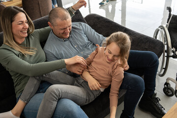 A father, facing physical challenges, engages in lively play with his family in the living room, creating cherished moments of joy and togetherness.	