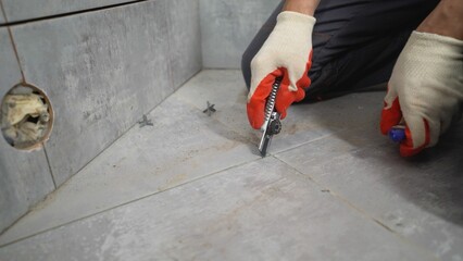 A man uses a trowel to remove old mortar. The concept of laying ceramic tiles in the bathroom. A...